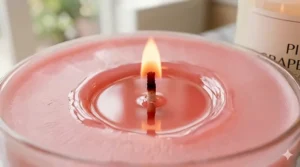 An extreme macro photograph of the burning cotton wick in a pink grapefruit soy candle, showing a pool of molten pink wax and a warm, clear flame.
